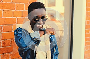 Portrait of stylish happy smiling african man with smart watch using voice command recorder or takes calling on city street