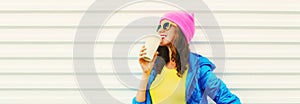 Portrait of stylish happy smiling young woman with cup of coffee wearing colorful pink hat, blue jacket on white background