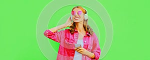Portrait of stylish happy smiling young woman in headphones with smartphone listening to music wearing pink jacket, sunglasses on