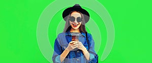 Portrait of stylish happy smiling young woman model with smartphone wearing black round hat, denim jacket on green background