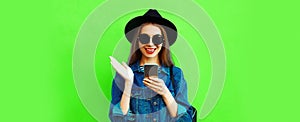 Portrait of stylish happy smiling young woman model with smartphone wearing black round hat, denim jacket on green background