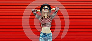 Portrait of stylish happy smiling young woman wearing black round hat on red background, blank copy space