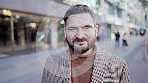 Portrait of stylish kind man with beard standing on city street and showing no head sign, negation gesture. Denying