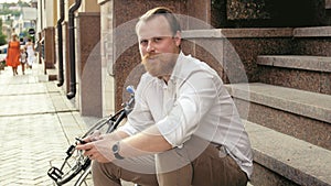 Portrait of young man with beard posing on stone staris at sunset