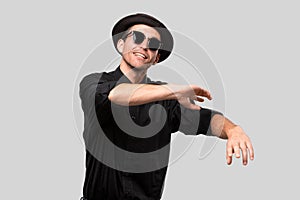 Portrait of a stylish man in a black shirt, pork pie hat and sun glasses over grey background