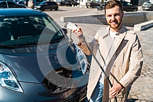 Portrait of stylish man with electric car charging connector in hands.