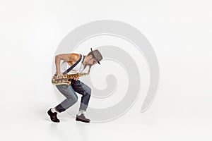 Portrait of stylish man in hat and suglasses playing saxophone , performing isolated over white background. Jazz
