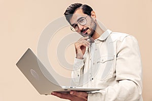 Portrait of a stylish man pensive look in glasses with a laptop in the hands of a freelancer, on a beige background in a