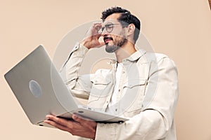 Portrait of a stylish man pensive look in glasses with a laptop in the hands of a freelancer, on a beige background in a