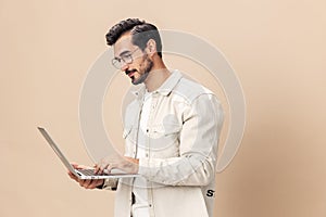 Portrait of a stylish man pensive look in glasses with a laptop in the hands of a freelancer, on a beige background in a