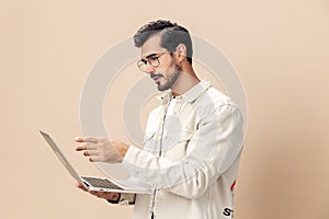 Portrait of a stylish man pensive look in glasses with a laptop in the hands of a freelancer, on a beige background in a