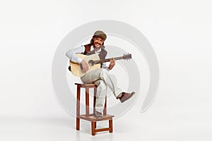 Portrait of stylish man playing guitar, performing isolated over white studio background. Smiling. Cheerful song