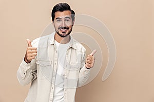 Portrait of a stylish man smile shows a class sign thumb up on a beige background in a white t-shirt, fashionable