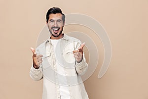 Portrait of a stylish man smile shows a class sign thumb up on a beige background in a white t-shirt, fashionable