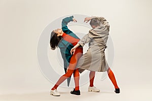 Portrait of stylish man and woman in coats and tights posing  over grey studio background. Weirdness, expression