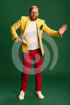 Portrait of stylish mature man in bright jacket and trousers isolated over green background. Concetp of fashion, beauty