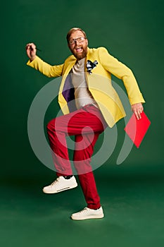 Portrait of stylish mature man in bright jacket and trousers isolated over green background. Concetp of fashion, beauty