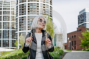 Portrait of stylish mature woman with gray hair on city street. Older woman in sunglasses waiting for public transport.