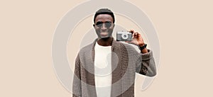 Portrait of stylish modern happy smiling young african man photographer with film camera taking picture isolated on gray