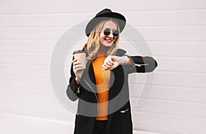 Portrait stylish smiling woman with smart watch using voice command recorder or takes calling holding coffee cup on city street