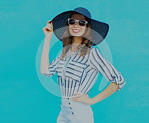 Portrait stylish smiling woman wearing a black round summer hat, white striped shirt on a blue background
