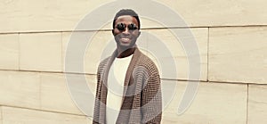 Portrait of stylish smiling young african man wearing brown knitted cardigan on city street background