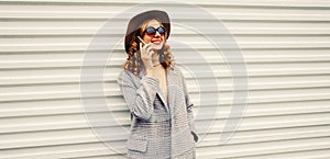 Portrait of stylish smiling young woman calling on smartphone wearing coat jacket and hat looking away on white background