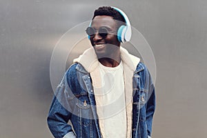 Portrait stylish urban smiling african man in headphones enjoying listening to music on gray metal wall background