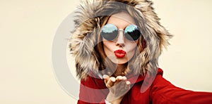 Portrait of stylish woman blowing her lips sends air kiss stretching hand for taking selfie with smartphone wearing jacket with