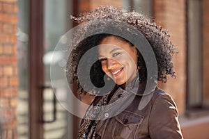 Portrait of stylish young African American woman flirtatious smiling and looking at camera. Brunette in brown leather