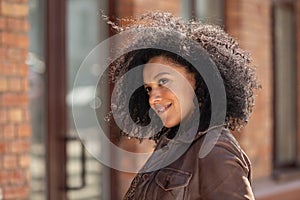 Portrait of stylish young African American woman flirtatiously biting her lip. Brunette with curly hair in brown leather
