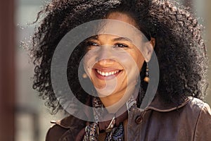 Portrait of stylish young African American woman smiling happily. Brunette with curly hair in brown leather jacket