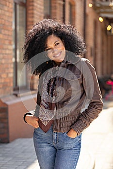 Portrait of stylish young African American woman smiling happily. Brunette with curly hair in brown leather jacket