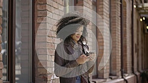 Portrait of stylish young African American woman viewing information on phone. Brunette in brown leather jacket posing