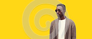 Portrait of stylish young african man model looking away wearing knitted cardigan isolated on yellow background, blank copy space