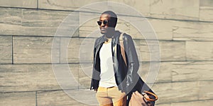 Portrait of stylish young african man model posing wearing black rock leather jacket with bag on city street background