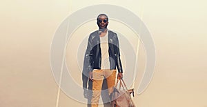 Portrait of stylish young african man model posing wearing black rock leather jacket with bag on city street background