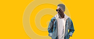 Portrait of stylish young african man model wearing denim jacket, backpack isolated on yellow background, blank copy space for