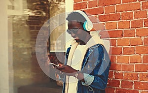 Portrait of stylish young african man with phone listening to music in wireless headphones on city street