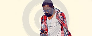 Portrait of stylish young african man with smartphone in earphones listening to music isolated on white background