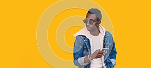 Portrait of stylish young african man with smartphone looking away isolated on yellow background, blank copy space for advertising