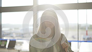 Portrait of a stylish young blonde girl traveller stands in airport terminal in sun light