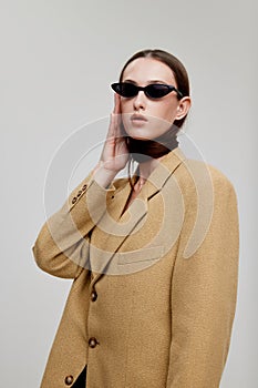 Portrait of stylish young girl posing in trendy sunglasses and oversized jacket isolated over grey background