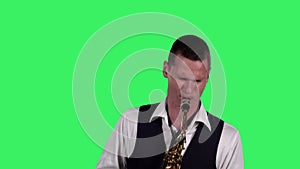 Portrait stylish young guy plays fast melody at saxophone on a green screen in the studio. Saxophonist performing a solo