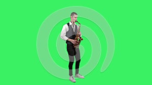 Portrait stylish young guy plays melody at saxophone on a green screen in the studio. Saxophonist performing a solo