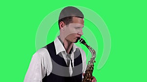 Portrait stylish young guy plays melody at saxophone on a green screen in the studio. Saxophonist performing a solo