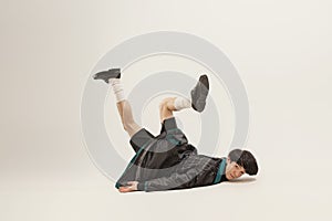 Portrait of stylish young man in black outfit and green coat falling on floor  over grey studio background