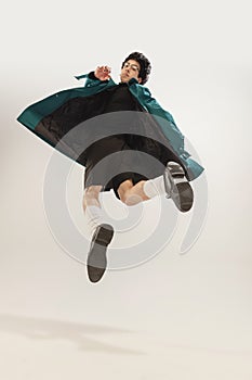 Portrait of stylish young man in black outfit and green coat posing in a jump  over grey studio background
