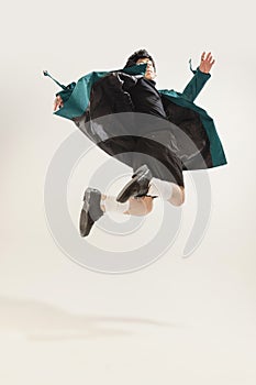 Portrait of stylish young man in black outfit and green coat posing  over grey studio background. Jumping