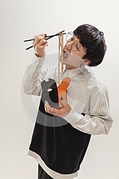 Portrait of stylish young man eating golden necklaces like noodles, posing  over grey studio background